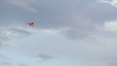 brightly coloured kite flying against a grey sky, low angle