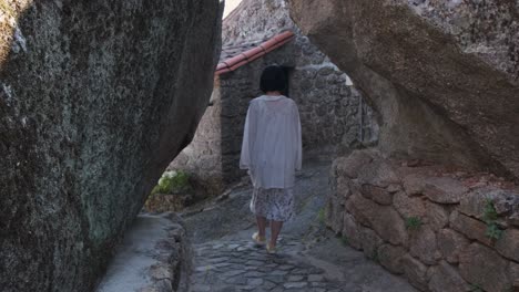 vista trasera de una mujer irreconocible caminando entre paredes rocosas del centro histórico de monsanto, portugal