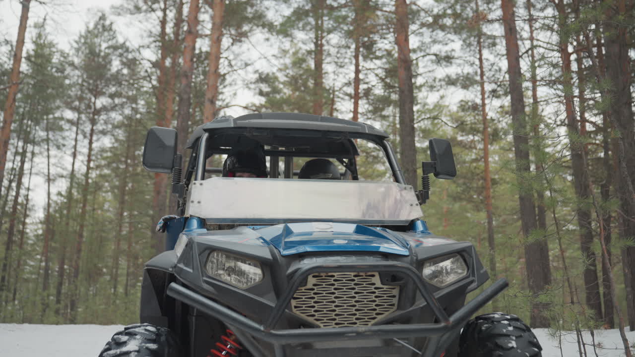Il conducente accende l'atv, i fari si illuminano. Il pilota in mimetica sale a bordo, le portiere si chiudono e il motore si accende con un rombo mentre il robusto buggy avanza su un sentiero di pini innevato, sospensioni e pneumatici che mordono la neve, intenso.
