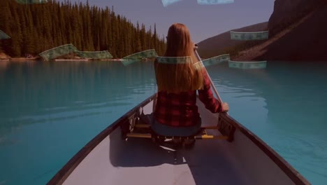 Rear-view-of-woman-boating-in-a-lake-against-american-dollar-bills-falling