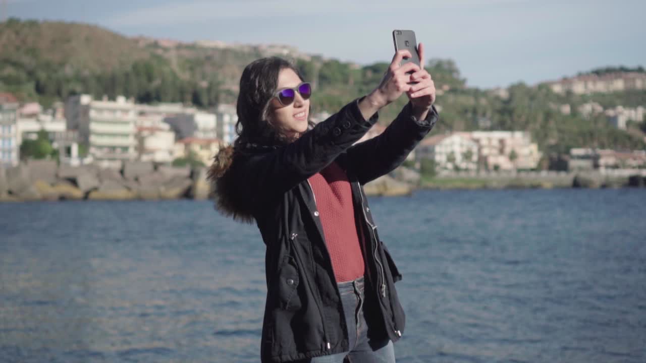 plano general de una chica tomando selfie y fotos con el mar de fondo en cámara lenta