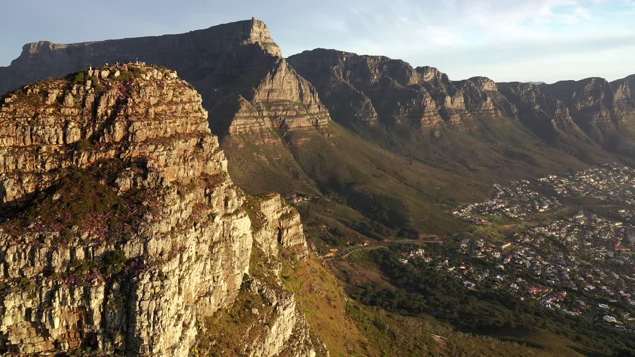 toma aérea cinematográfica del pico de cabeza de león de ciudad del cabo que revela el parque nacional de la montaña de la mesa y la bahía de campamentos durante la puesta de sol de la hora dorada