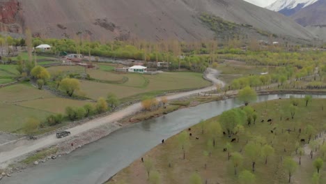 aerial above suv along rural road beside river in ghizer valley district in pakistan