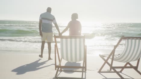 Feliz-Pareja-Afroamericana-Senior-Caminando-Y-Tomándose-De-La-Mano-En-La-Playa,-En-Cámara-Lenta