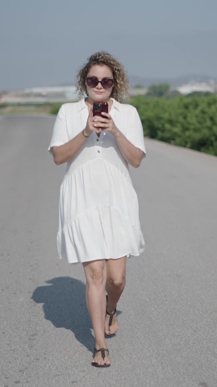 Donna con vestito bianco che usa un cellulare su una strada