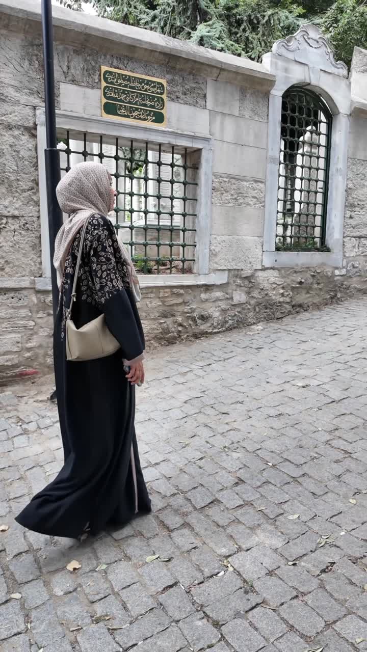 Woman in Hijab and Abaya Walking Along Historic Stone Wall