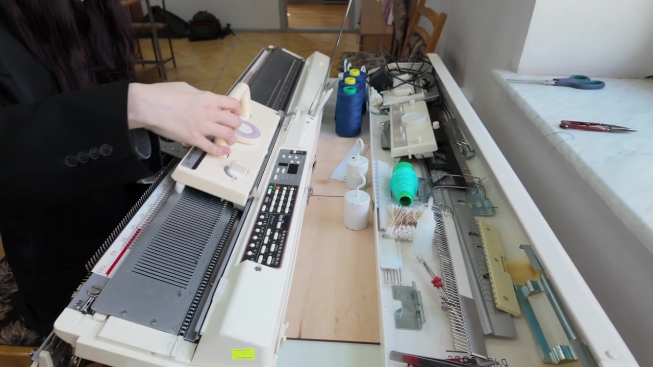 Close up of an industrial or semi professional knitting machine, focusing on the metal needle bed and carriage