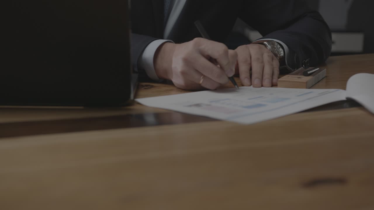 Uomo d'affari firma documenti vicino al laptop su un tavolo di legno
