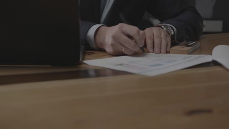 businessman signs papers near laptop on wooden table