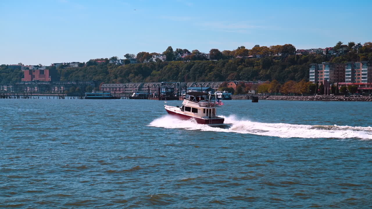 New York, USA, 1 novembre 2025: motoscafo che sfreccia velocemente sull'Hudson, lasciando una scia bianca ben visibile. L'assolata scena grandangolare mostra il motoscafo sullo sfondo di case e alberi verdi sulle Palisades del New Jersey.