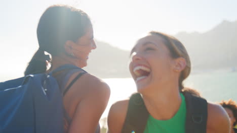 Grupo-De-Amigas-Con-Mochilas-Ayudándose-Mutuamente-En-Una-Caminata-En-El-Campo-Por-La-Ruta-Costera