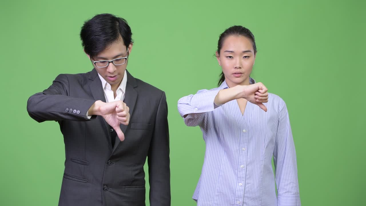 Young Asian business couple giving thumbs down together