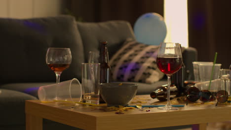 cerrar el salón desordenado o la sala de estar con la mesa cubierta con vasos de vino vacíos y botellas de cerveza después de la fiesta de la casa