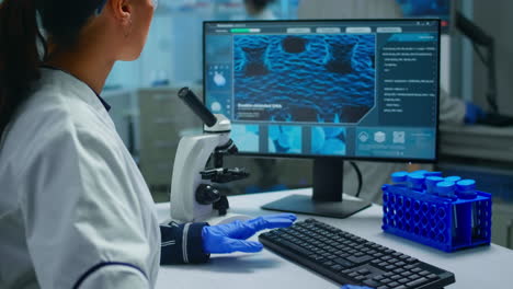 bioquímico usando el microscopio y escribiendo en la computadora trabajando en un laboratorio equipado