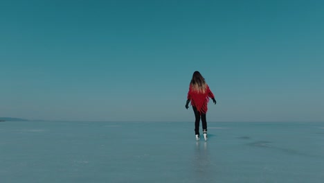 Tracking-back-shot-of-a-girl-ice-skating-on-a-frozen-lake-wearing-a-red-shawl,-on-a-clear-sunny-day,-serene-moments