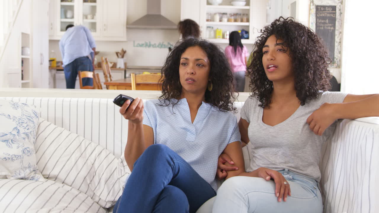 Mor med teenage datter sidder i sofaen og ser tv sammen