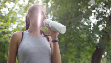 Retrato-De-Una-Chica-Bastante-Deportiva-Bebiendo-Agua-Después-De-Su-Sesión-De-Carrera-Y-Mirando-La-Cámara