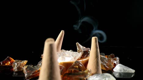 static shot of unlit incense cones in a decorative rock garden, a lit cone w- smoke flowing in the back