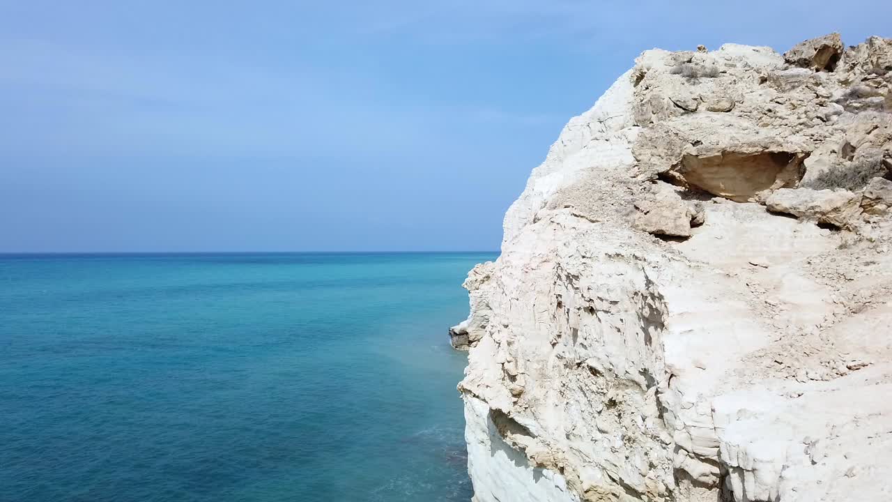 Crystal blue sea crashes gently against rocks under a clear sky. This coastal scene captures the peaceful rhythm and natural beauty of the Cyprus white rocks shoreline.