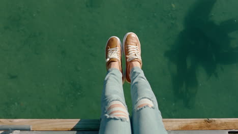 top-view-woman-legs-dangling-over-water-girl-enjoying-summer-vacation-sitting-on-seaside-beach-jetty