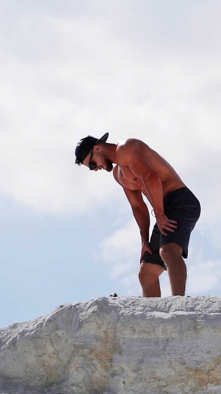 Young man contemplating after training. Young sportive male resting on top of mountain Vertical video