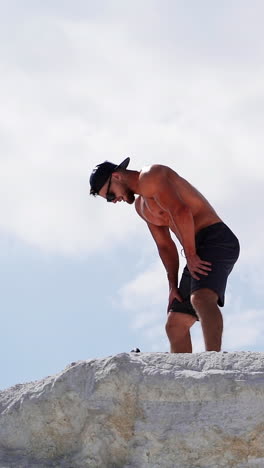 young man contemplating after training. young sportive male resting on top of mountain vertical video