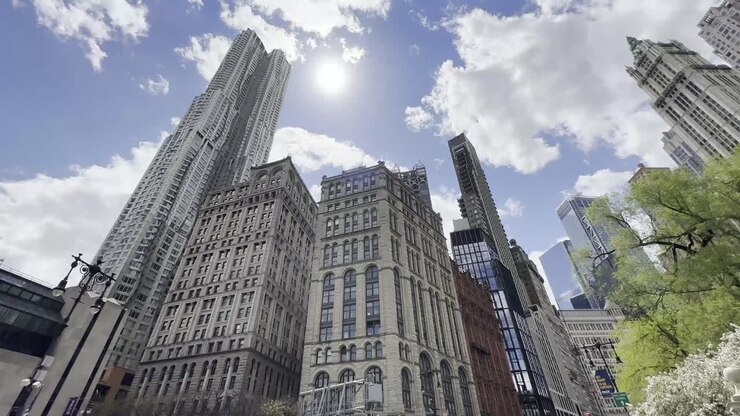Um dia claro e ensolarado em Manhattan com céus azuis límpidos, destacando a arquitetura deslumbrante dos arranha-céus icônicos da cidade e árvores verdes exuberantes.