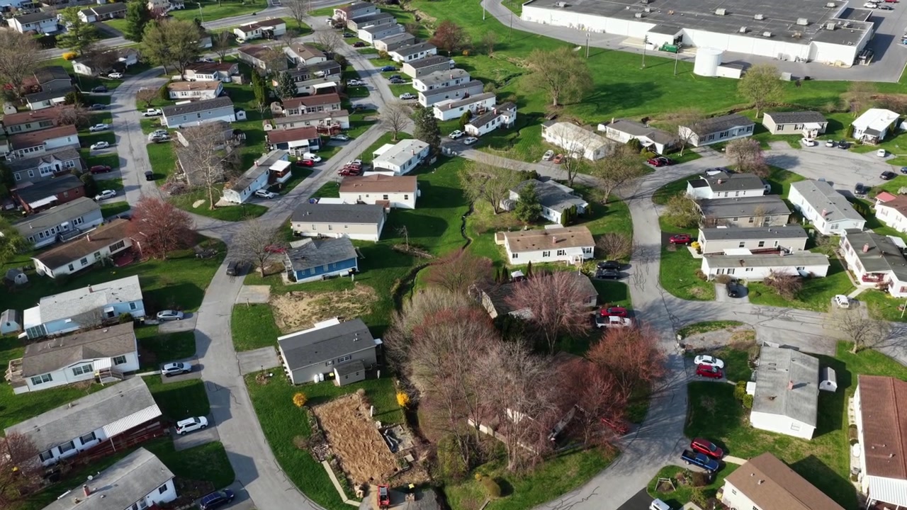 Quartiere residenziale suburbano curvo con case a un piano e case mobili ad Akron, PA, circondato da verde primaverile, strade tranquille e una disposizione organizzata. Vita residenziale accessibile. Sorvolo aereo