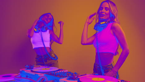 identical twin female djs dancing behind record turntables