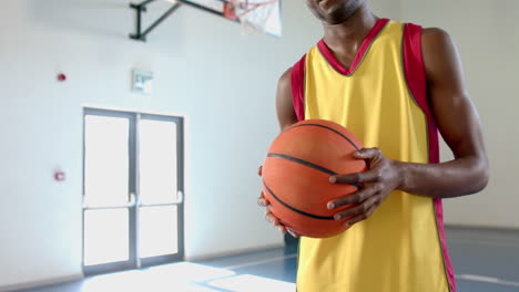 young african american man holds a basketball in a gym, with copy space