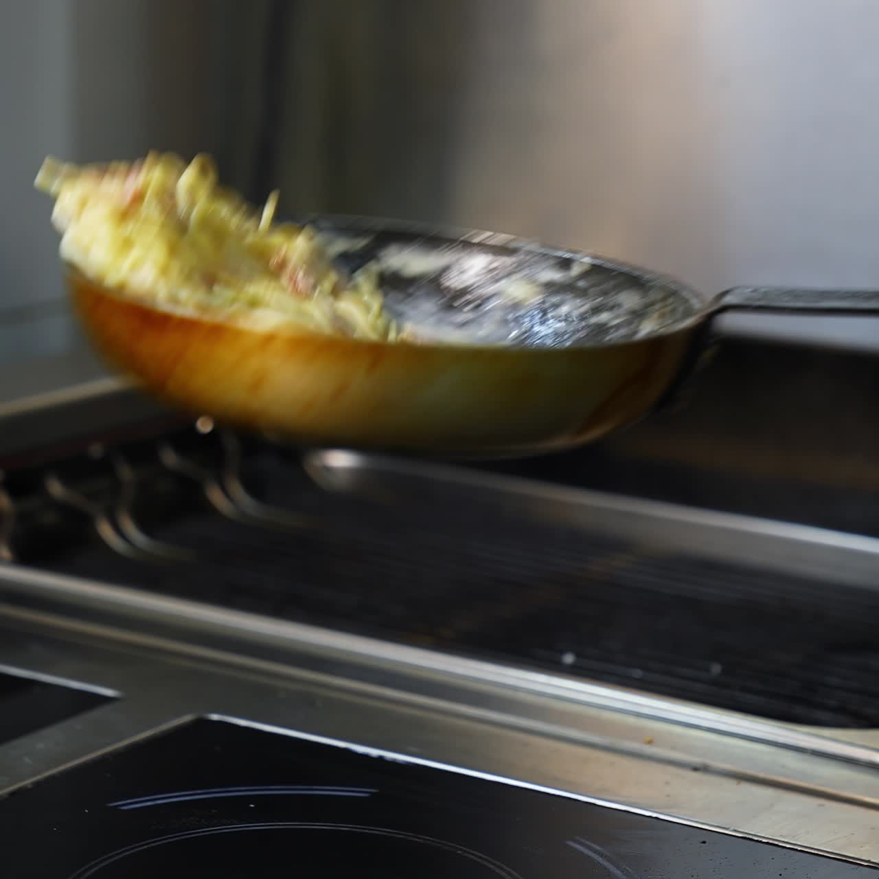 Cooking meals in a restaurant. Chef is cooking dish in a frying pan and flipping throwing it. Cooking the spaghetti in white sauce in the frying pan. Close-up