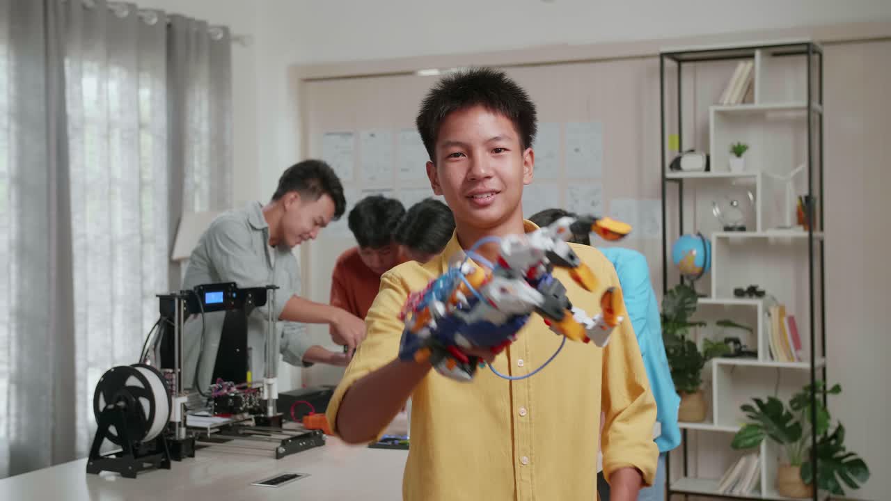 3d 프린팅과 노트북을 가진 젊은 아시아 소년 그룹, 사이보그 손으로 미소 짓는 소년, 몸짓을 보여주고 팔을 교차하는 동안 그의 친구들은 집에서 일에 대해 논의합니다.