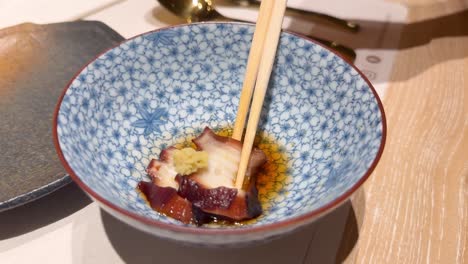 chopsticks lifting octopus with wasabi from bowl