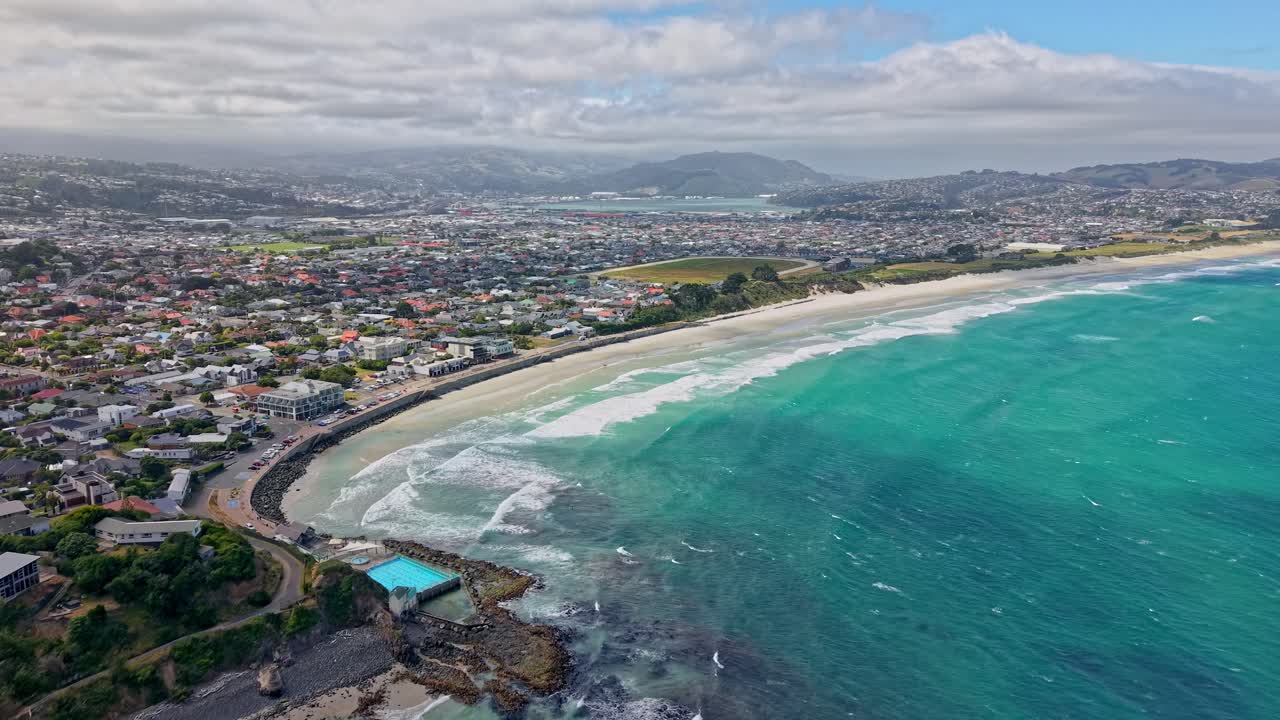 Drone flies over St Clair Beach showing city, waves, and coastal hills
