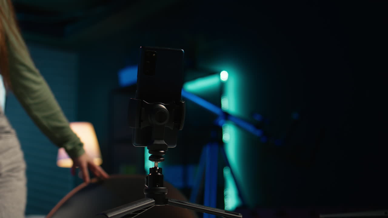 una chica feliz llegando al estudio, filmando un vlog con un teléfono inteligente en un trípode