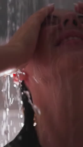 la mujer se relaja en los aerosoles de agua de la ducha de cerca. la dama bonita con los ojos cerrados y el cabello mojado disfruta de los aerosoles refrescantes en el baño. procedimientos de cuidado de spa