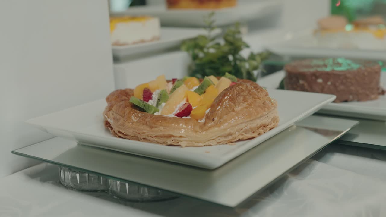 밝은 색상의 디저트 스탠드 위에 신선한 과일 조각이 왕관처럼 올려진, 겉은 바삭하고 속은 촉촉한 황금색 페이스트리