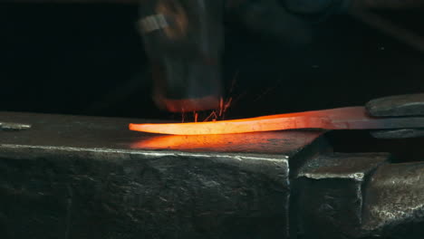 macro shot of forge hammering on glowing iron inside workshop