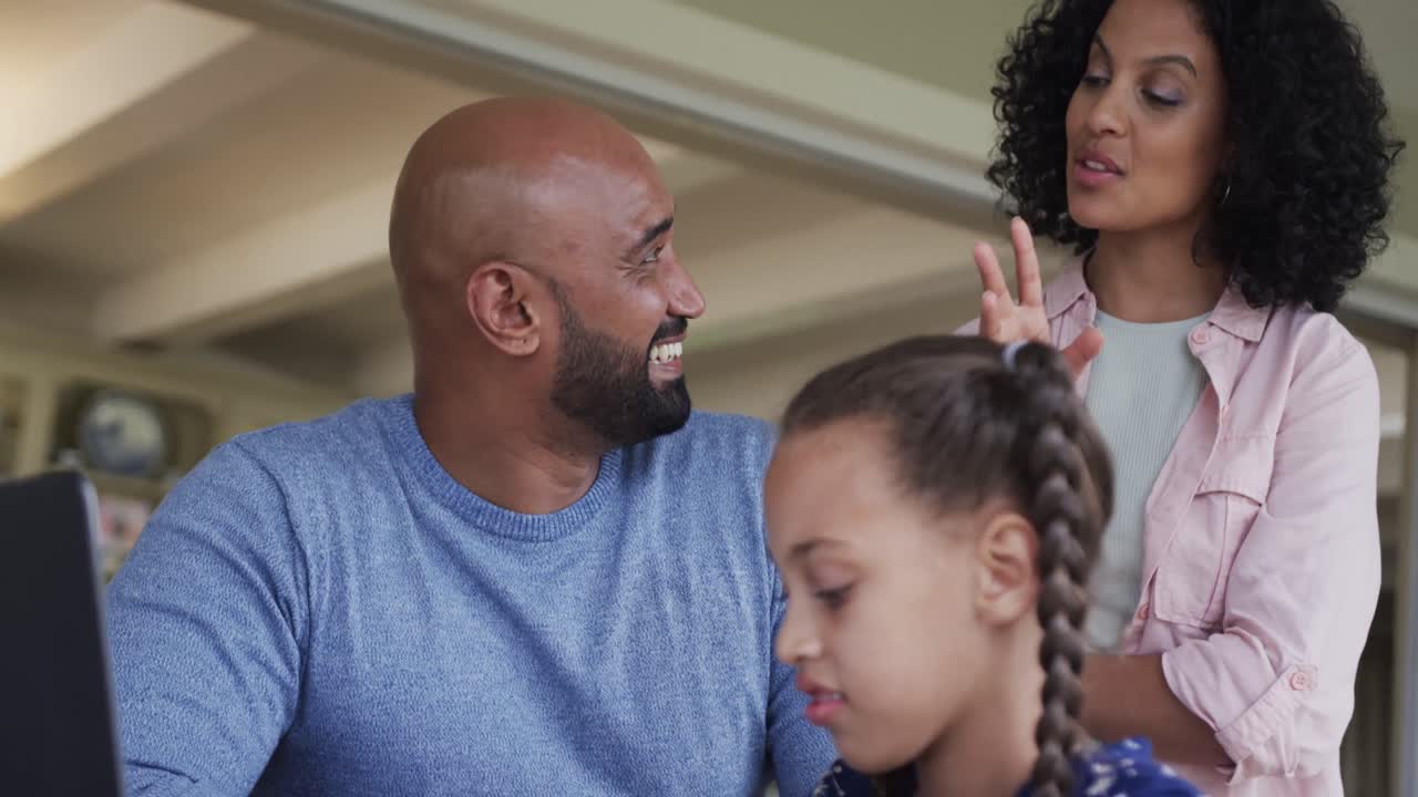 Happy biracial parents and daughter learning online using laptop at table, slow motion