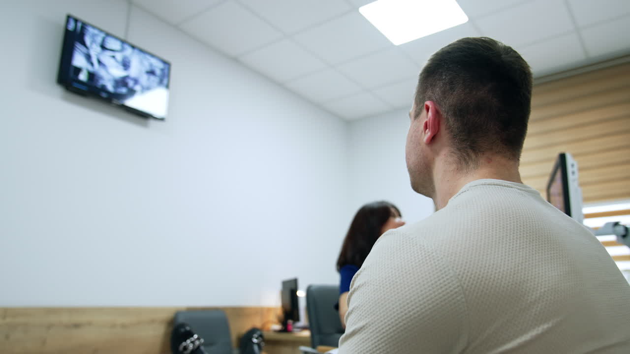 Rear view of a man sitting in the cabinet of a doctor. Man observes on the monitor the process of ultrasound check of his pregnant wife. Low angle view.