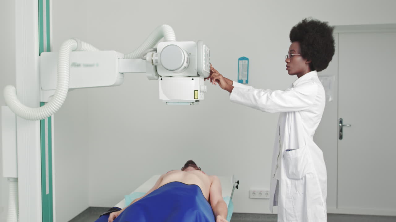 In the hospital man lying on a bed female technician adjusts xray machine scanning for fractures