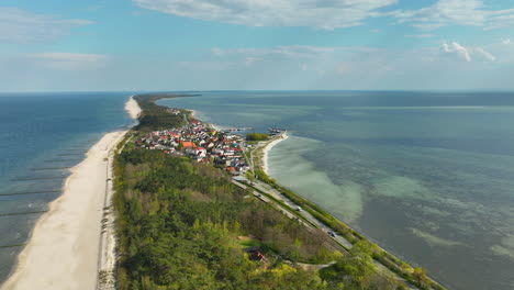 Luftaufnahme-Von-Kuźnica,-Polen,-Mit-Einem-Schmalen-Landstreifen,-Der-Auf-Der-Einen-Seite-Vom-Meer-Und-Auf-Der-Anderen-Seite-Von-Der-Bucht-Begrenzt-Wird,-Mit-Einer-Lebendigen-Gemeinde-Dazwischen