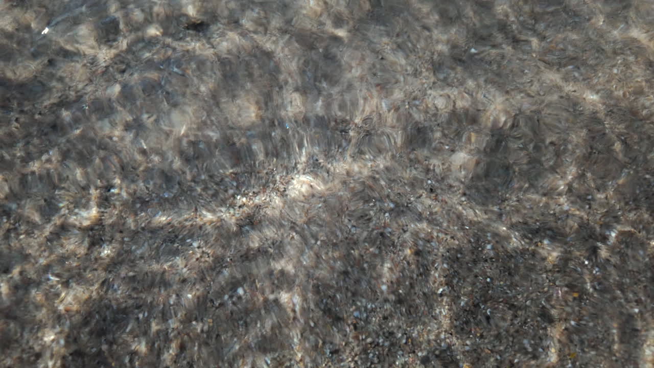 Calm underwater view showing sand ripples and light reflections beneath the sea surface