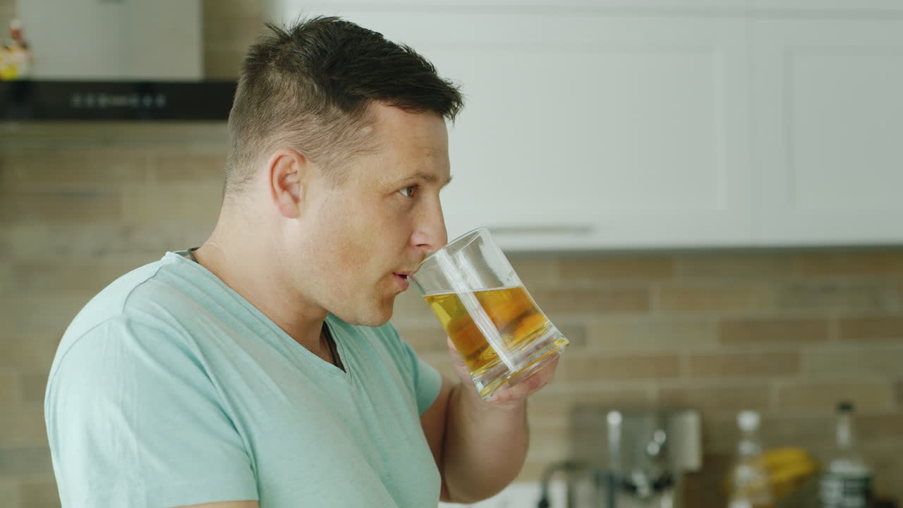 un joven caucásico bebe cerveza en su cocina