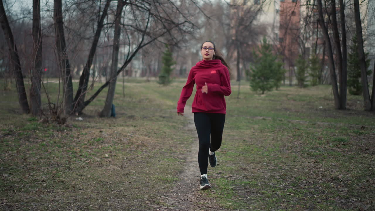 Donna bianca che corre in un parco urbano, esercizio di scatto con personal trainer, tragitto giornaliero di uno studente, intervallo con health coach, antistress per impiegato, servizio fotografico di una modella, recupero di un jogger consapevole. Mattinata nuvolosa