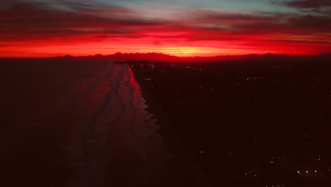 Breathtaking-tilting-aerial-shot-of-beach-and-ocean-in-crazy-red-burning-sky-sunset,-Brazil