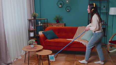 Joyful-young-woman-is-mopping-floor-in-apartment-living-room,-having-fun-listening-to-music-at-home