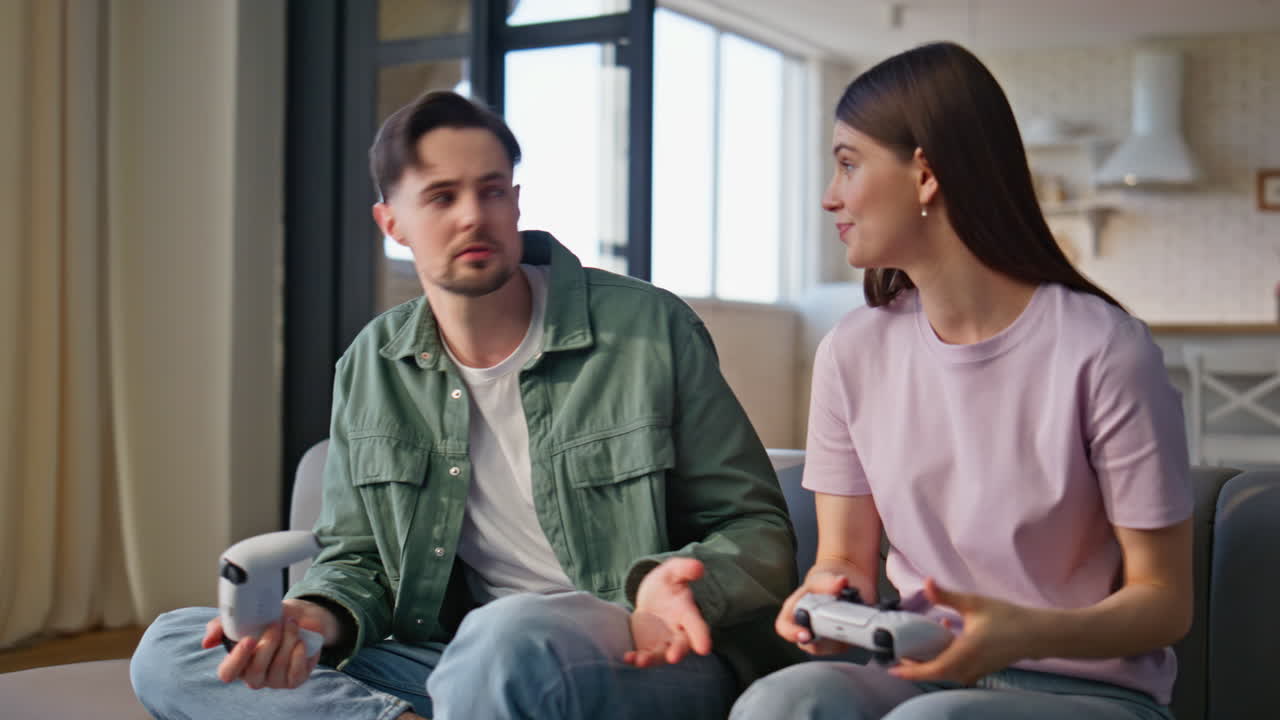 Emotional players competing online sitting sofa with console at home closeup