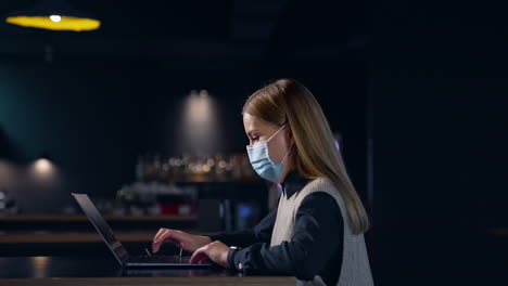 Woman Working on Laptop in Night Restaurant with Mask
