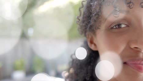 Animation-of-light-spots-over-half-portrait-of-happy-biracial-teenage-girl-smiling-in-garden